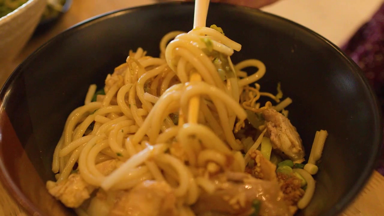 Primo piano di bacchette che sollevano saporiti noodles di riso Mee Shay birmani da una ciotola