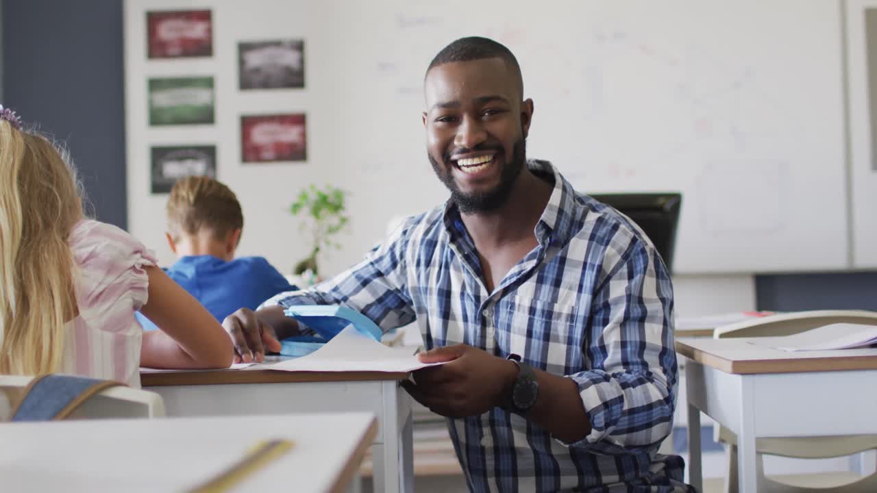 Video of happy african american male teacher helping pupils during lessons
