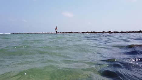 pescador lanzando un anzuelo en una línea mientras está de pie sobre los arrecifes de coral en marea alta con un viento que sopla a través del mar de andaman hacia la orilla