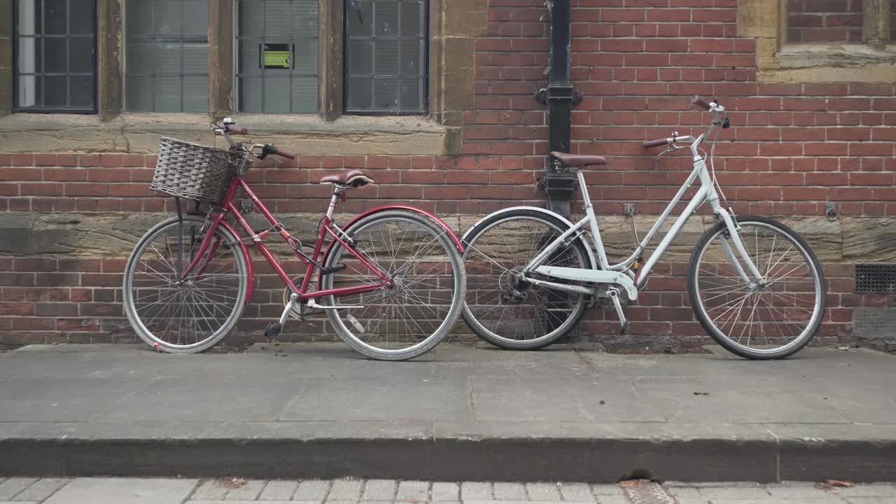 Two vintage bicycles parked against a red brick wall of a building in Cambridge city, England