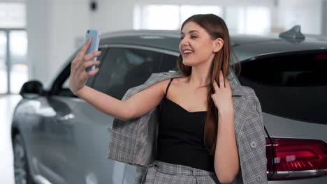 stylish adult girl in a business suit takes a selfie on a smartphone with a car