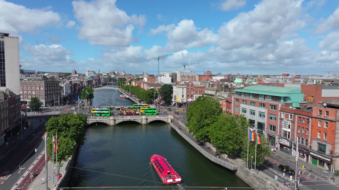 Rosa Ausflugsboot fährt unter zwei Straßenbrücken an einem hellen Tag mit Verkehr, Bussen und Fußgängern im Zentrum von Dublin.