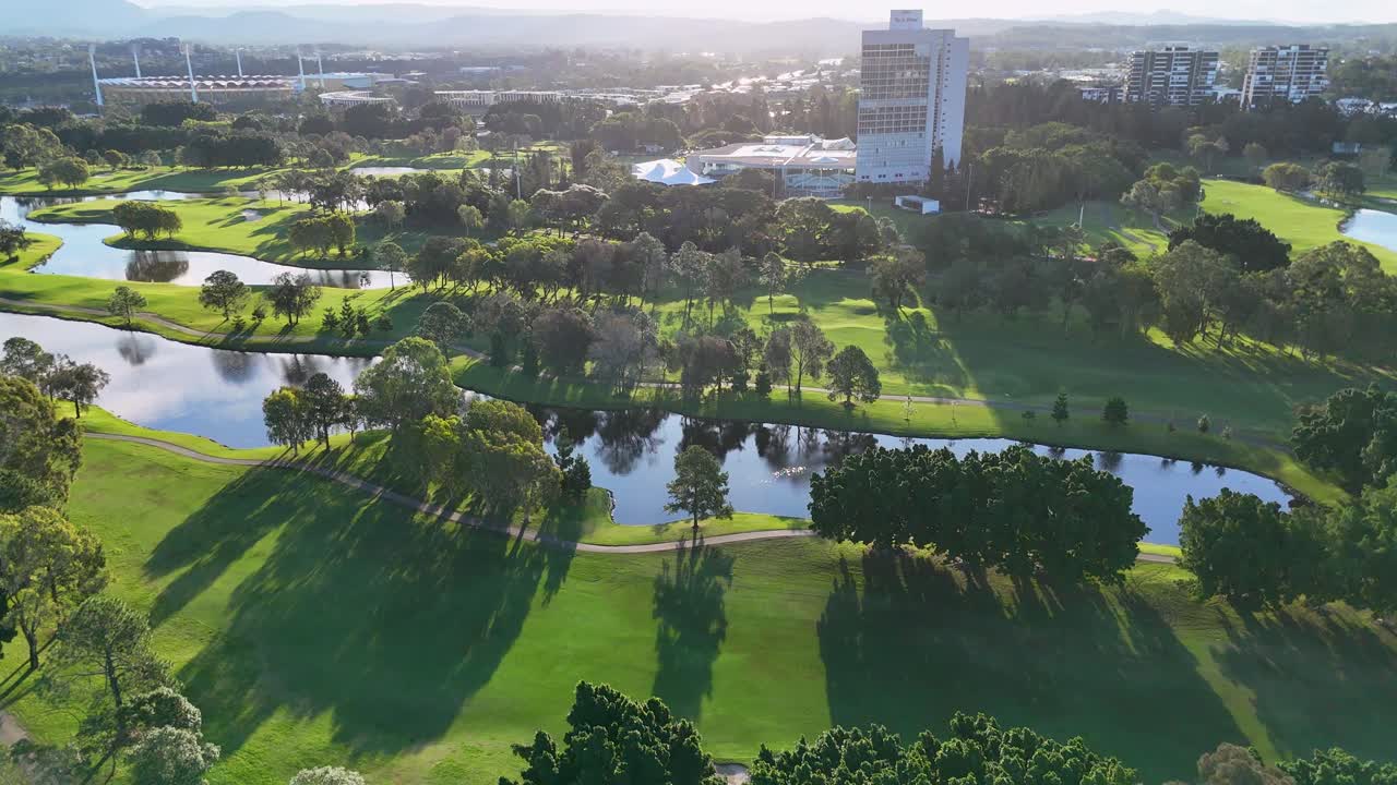 Drone captures lush golf course landscape with water hazards and trees under warm sunset lighting