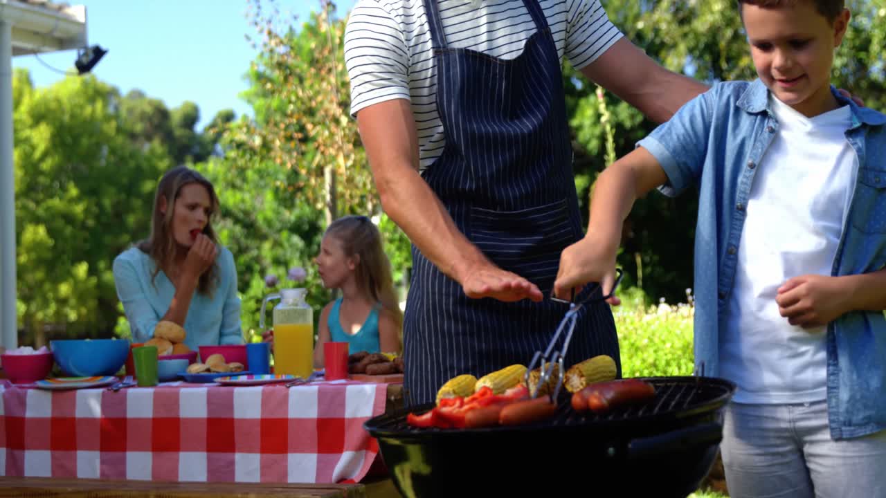 Padre e figlio che grigliano salsicce e pannocchie al barbecue