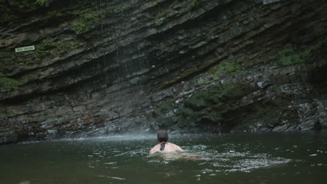 woman swimming under a waterfall in a natural pool