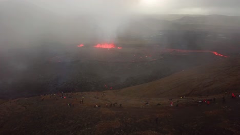 aerial landscape view of people looking at fagradalsfjall volcano erupting, with lava flowing across the meradalir valley floor