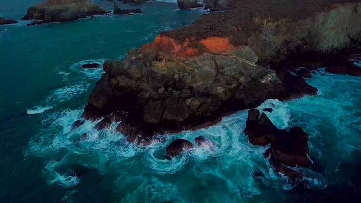 Órbita lenta alrededor de un promontorio rocoso azotado por las olas en la Playa Sand Dollar en Big Sur, California, al anochecer.