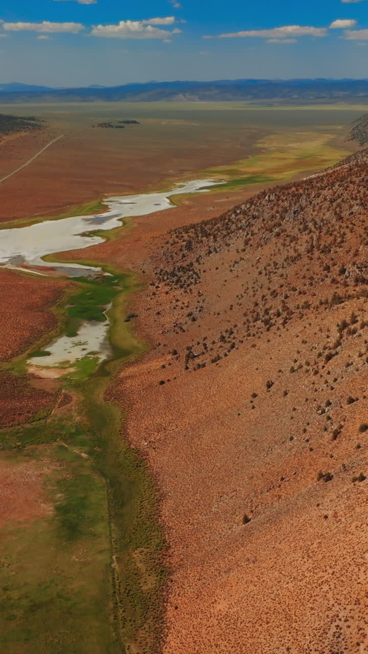 Dry sandy landscape of Nevada, United States on sunny day. Rocky hills with some puddles surrounded by scarce greenery from top view. Vertical video
