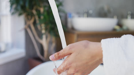 Mid-section-of-mixed-race-woman-washing-her-hands-in-bathroom