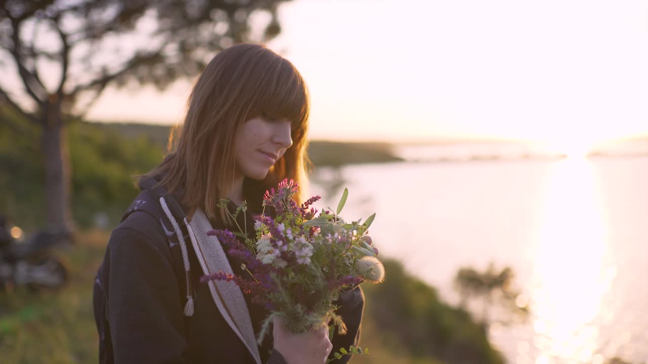 hermosa mujer joven con un ramo de flores silvestres en la costa al atardecer