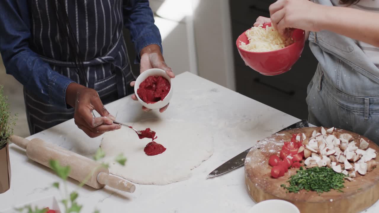 Midsection of diverse teenage female friends preparing pizza base, in slow motion