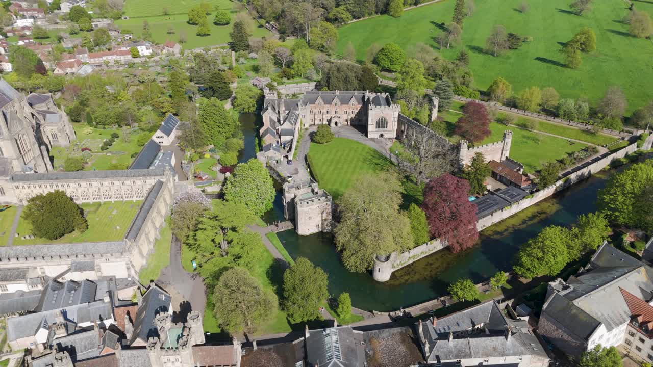 Aerial glide over moated Bishop’s Palace with crenellated stone walls, towers and manicured lawns surrounded by mature trees for an atmospheric heritage scene