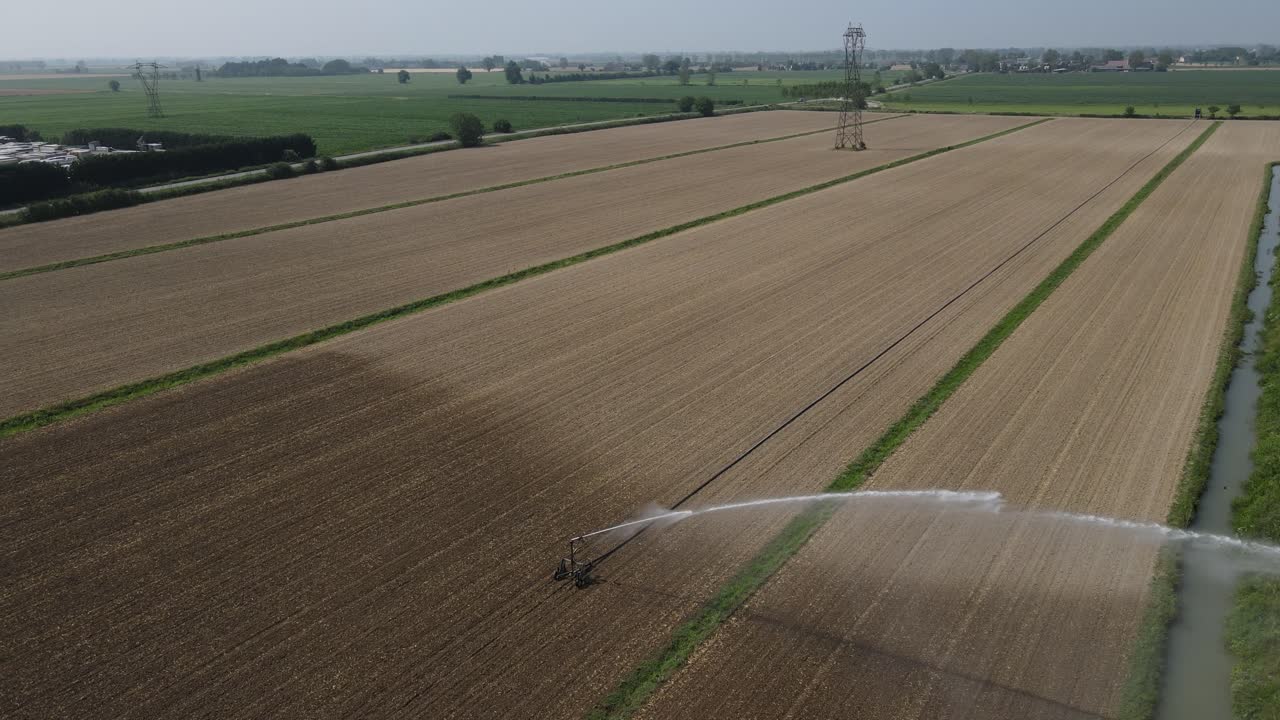 Aerial drone footage with a clockwise rotation tracking a rainbow in the water spray of a farmland sprinkler in Italy, gradually pulling back and ending with a scenic reveal of the landscape