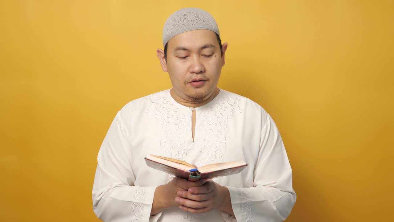 젊은 아시아 무슬림 남성의 초상화, 노란색 배경에 대한 거룩한 꾸란을 읽는, 이슬람 주제, 라마단 카림 또는 이드 무바라크