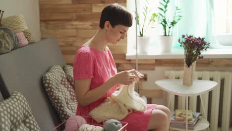 mujer creativa tejiendo lana sentada en el sofá en la ventana de fondo