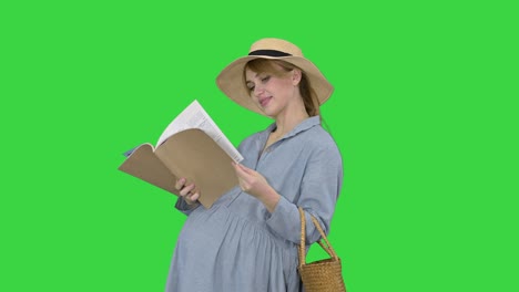 pregnant woman in a summer hat reading magazine on a green screen, chroma key