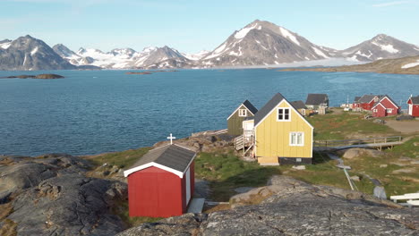 peaceful and colorful seaside village in greenland with snow capped mountains in distance and small homes in foreground with tiny red church