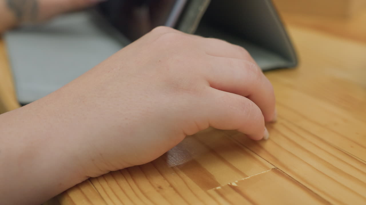 close up of woman hand with fixed polished nails gently tapping on wooden table near digital tablet in cozy indoor space creating subtle movement with delicate nail design and calm reflective mood