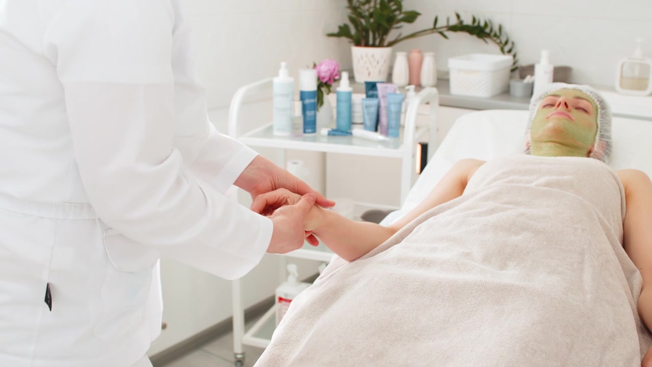 Kosmetikerin gibt einer Frau eine entspannende Handmassage während einer Gesichtsmaskenbehandlung im Beauty-Spa.