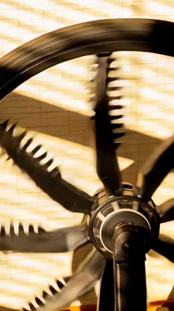 Video verticale: Ventilatore da soffitto con mozzo metallico che gira, producendo una sfocatura delle pale seghettate per tutta la stanza, con tende.