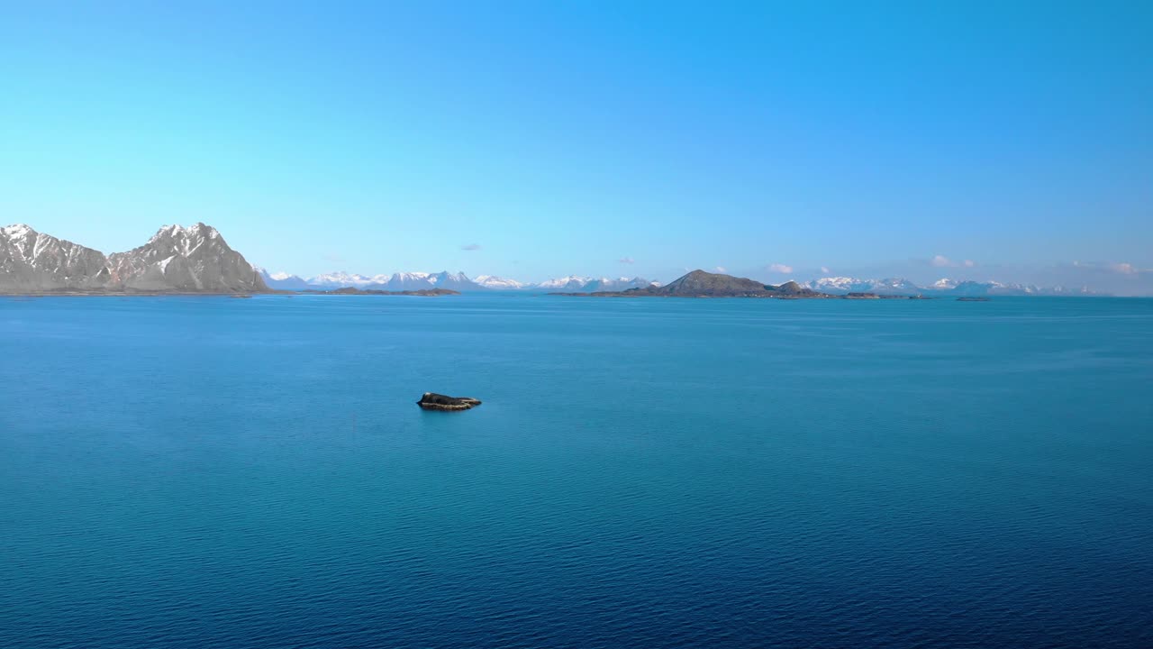 Aerial drone shot of the blue ocean in Lofoten, Norway and mountains in the background.