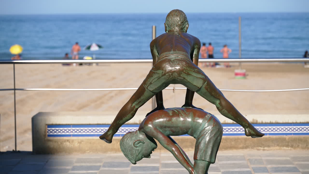 Alicante, Spain - May 24, 2025: Bronze statue of kids playing leap-frog on the palm-lined promenade at Playa de San Juan