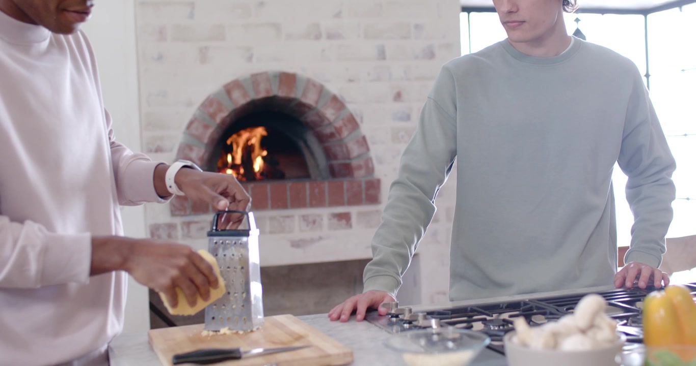 Amici maschi, un adolescente e un trentenne, prendono una grattugia e grattugiano il formaggio con una spugna in cucina per la pizza