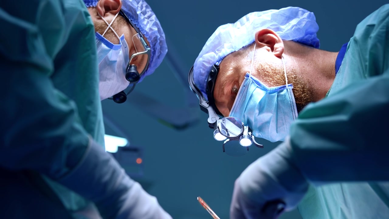 Medici con occhiali ingranditori chirurgici eseguono un intervento di chirurgia maxillo-facciale. Vista dal basso sui chirurghi concentrati sul loro lavoro.