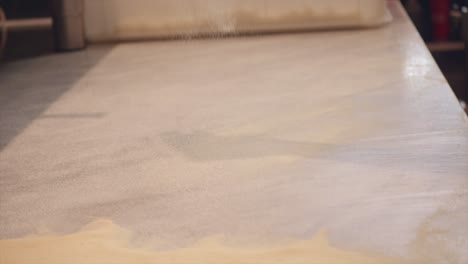 la harina de pizza se extiende sobre la mesa de fabricación de la masa de pizza