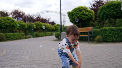 sweet little baby boy looks on the soap bubbles. kid tries to catch the bubbles in the park.