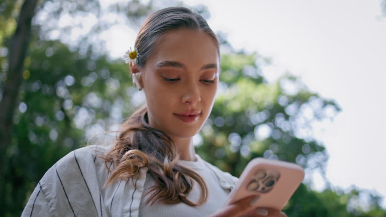 mujeres tranquilas con auriculares caminando por el bosque verde soleado mirando el teléfono inteligente de cerca.