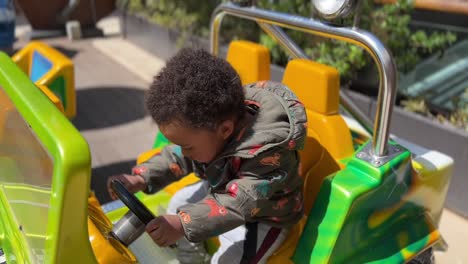 two year old exotic  afroeuropean child enjoying in a slot toy car, wearing a green jacket