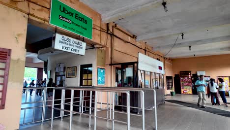 kandy railway station's exit area featuring a ticket booth, exit sign, and various signage. the scene captures the transport hub's lively atmosphere in sri lanka.