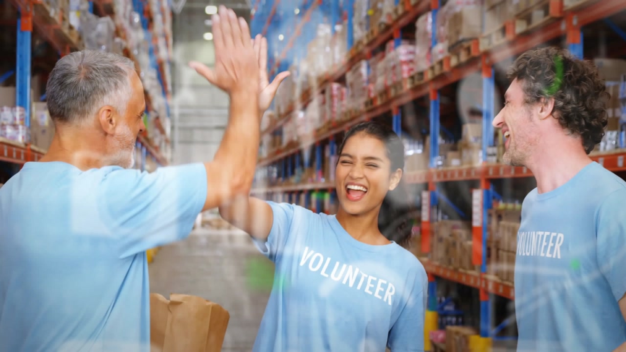 Animation of digital icons over diverse volunteers high fiving in warehouse