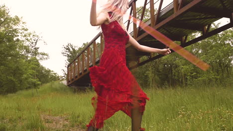 young blonde woman in a red dress dances around a meadow with twirling a ribbon wand