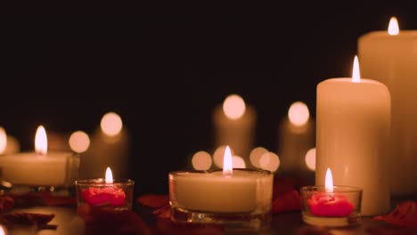 eye level shot of romantic lit candles on black background covered in rose petals with copy space 1