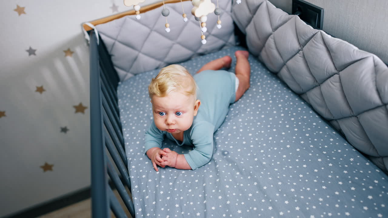 Beautiful peaceful infant boy lies in the cot. Lovely baby in the crib under the mobile.