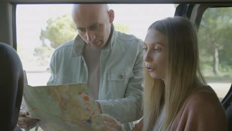 focused couple discussing map at car