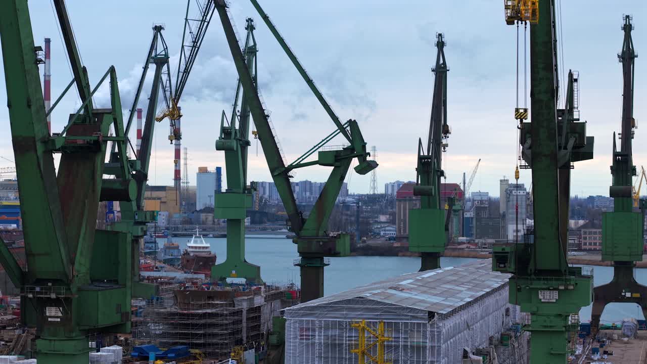 Aerial flythrough of Gdansk Shipyard, ships, cranes, coal plant, and industrial construction areas, city skyline on opposite side of river