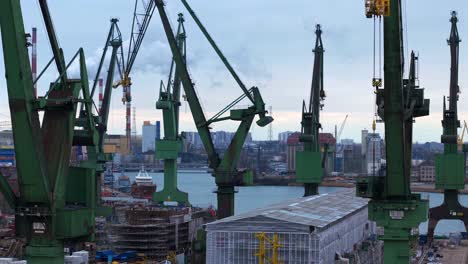 aerial flythrough of gdansk shipyard, ships, cranes, coal plant, and industrial construction areas, city skyline on opposite side of river