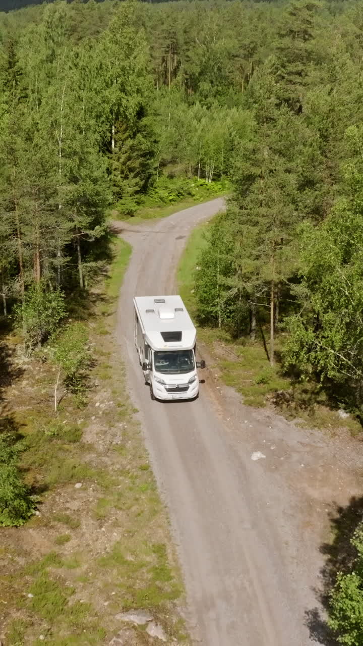 Vertical drone shot in front of a RV on a forest, dirt road in the Nordics