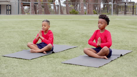 multiracial boys practicing yoga on mats on school field, focusing and relaxing