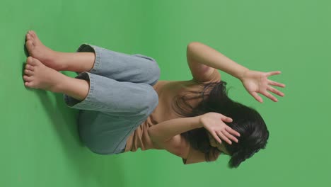 full body of young asian woman victim of violence with bruise on body making defending gesture and fearing while sitting in the green screen background studio