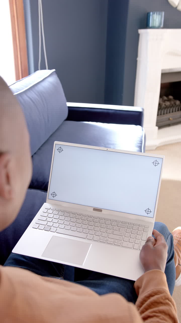 Vertical video of african american man using laptop with copy space on screen at home, slow motion