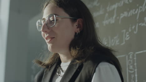 young person with glasses in front of a chalkboard