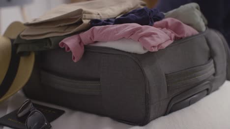 close up of person packing clothes into suitcase ready for summer holiday