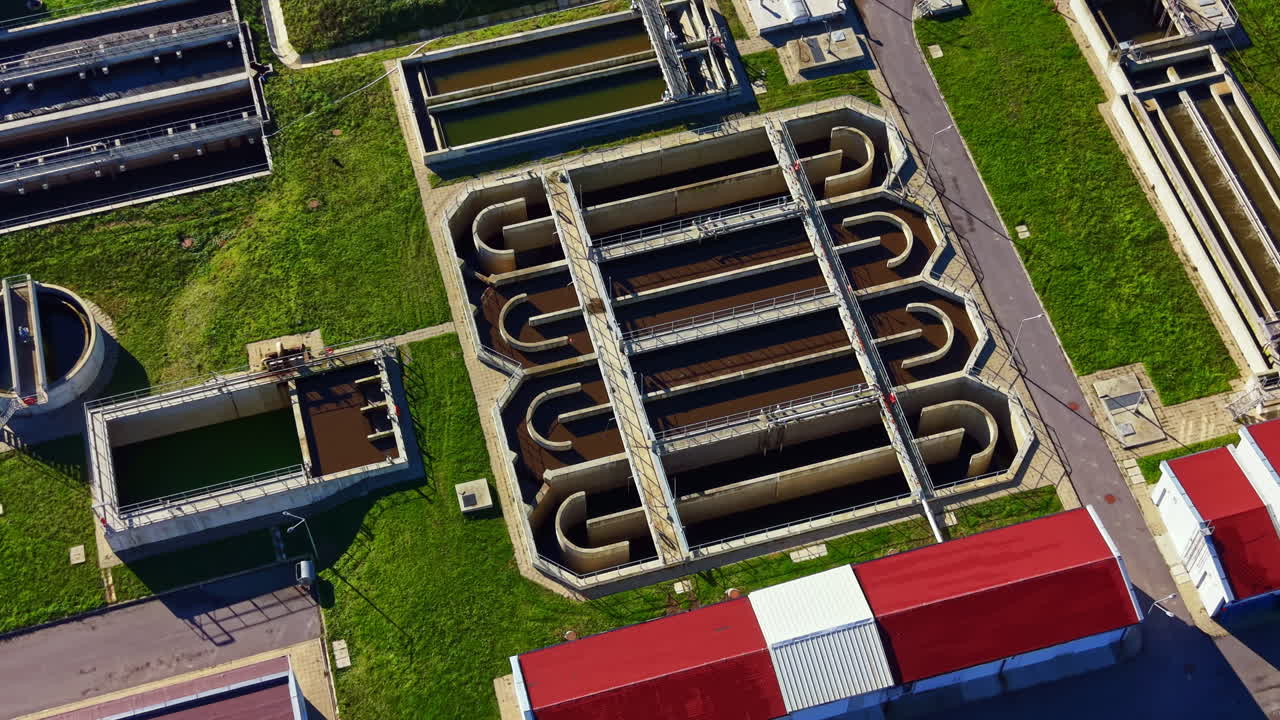 Overview of a water treatment facility showing tanks and channels during the day with green grass and building structures visible from above