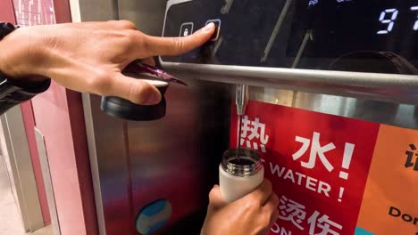 person refills travel mug from public hot water dispenser