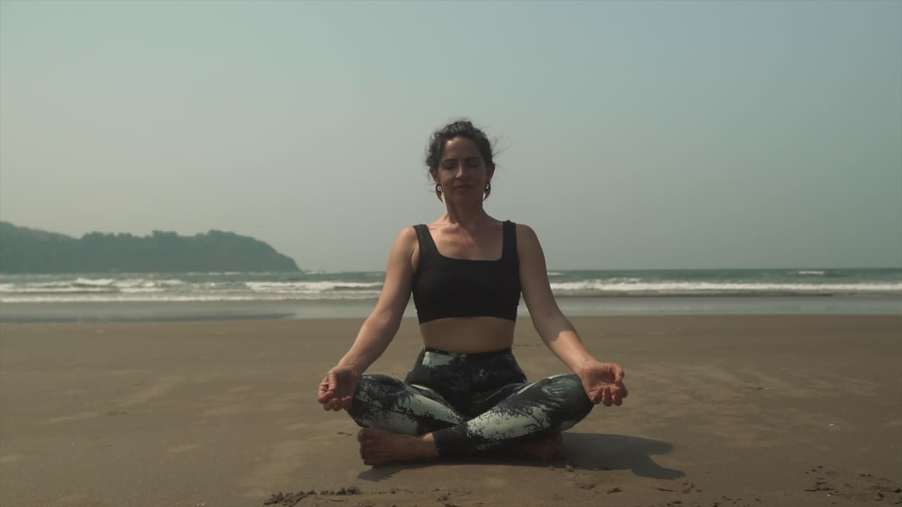 mujeres meditando en la playa con la cabeza inclinada hacia adelante mientras se relaja en la práctica