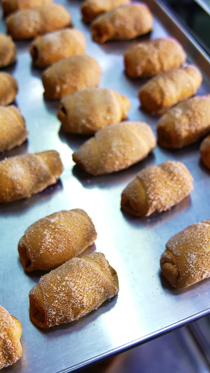 Metal baking sheet filled with freshly baked little croissants. Close up. Sweet desserts production at modern bakery. Vertical video